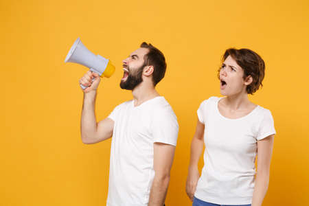 Bewildered young couple friends bearded guy girl in white blank empty t-shirts isolated on yellow orange background.の写真素材