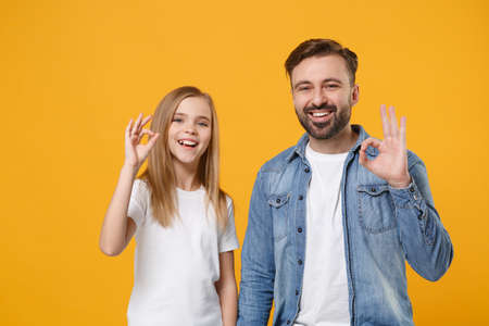 Funny bearded man in casual clothes have fun with child baby girl. Father, little kid daughter isolated on yellow orange background. Love family day parenthood childhood concept. Showing OK gesture.の写真素材