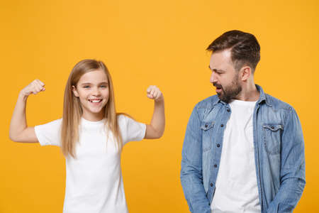 Bearded man in casual clothes have fun with cute strong child baby girl. Father little kid daughter isolated on yellow background. Love family day parenthood childhood concept. Showing biceps muscles.の写真素材