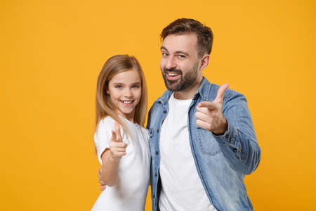 Smiling bearded man in casual clothes with cute child baby girl. Father little kid daughter isolated on yellow background. Love family day parenthood childhood concept. Point index fingers on camera.の写真素材