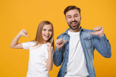 Laughing bearded man in casual clothes with cute child baby girl. Father little kid daughter isolated on yellow background. Love family day parenthood childhood concept. Pointing thumbs on themselves.の写真素材