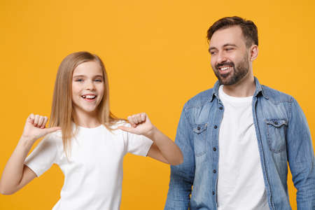 Smiling bearded man in casual clothes have fun with child baby girl. Father little kid daughter isolated on yellow background. Love family day parenthood childhood concept. Pointing thumbs on herself.の写真素材