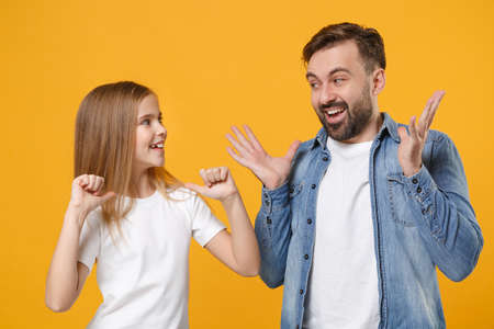 Funny bearded man in casual clothes with child baby girl. Father little kid daughter isolated on yellow background. Love family day parenthood childhood. Pointing thumbs on herself, spreading hands.の写真素材