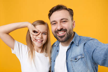 Close up of bearded man with child baby girl. Father little kid daughter isolated on yellow background. Love family day parenthood childhood. Doing selfie shot on mobile phone, holding hand near eye.の写真素材
