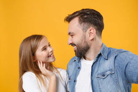 Close up of bearded man with child baby girl. Father little kid daughter isolated on yellow background. Love family day parenthood childhood. Doing selfie shot on mobile phone, looking at each other.の写真素材