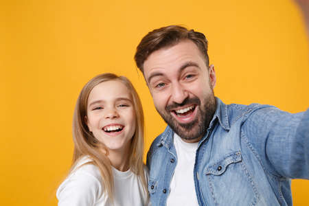 Close up of laughing bearded man with cute child baby girl. Father little kid daughter isolated on yellow background. Love family day parenthood childhood concept. Doing selfie shot on mobile phone.の写真素材