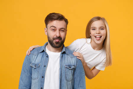Cheerful bearded man in casual clothes have fun with cute child baby girl. Father little kid daughter isolated on yellow wall background. Love family day parenthood childhood concept. Showing tongue.の写真素材