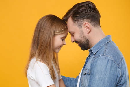 Side view of bearded man in casual clothes have fun with child baby girl. Father little kid daughter isolated on yellow background. Love family day parenthood childhood concept. Touching foreheads.の写真素材