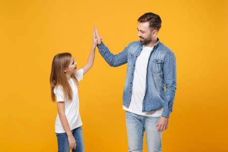 Cheerful bearded man have fun with cute child baby girl. Father little kid daughter isolated on yellow background. Love family day parenthood childhood concept. Giving high five, holding hands folded.の写真素材