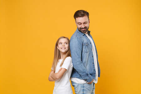 Pretty bearded man in casual clothes have fun with cute child baby girl. Father little kid daughter isolated on yellow background. Love family day parenthood childhood concept. Standing back to back.の写真素材