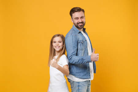 Smiling bearded man in casual clothes with child baby girl. Father little kid daughter isolated on yellow background. Love family day parenthood childhood concept. Stand back to back showing thumb up.の写真素材