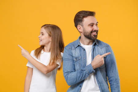 Cheerful bearded man in casual clothes have fun with child baby girl. Father little kid daughter isolated on yellow background. Love family day parenthood childhood concept. Point index fingers aside.の写真素材