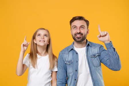Pretty bearded man in casual clothes have fun with child baby girl. Father little kid daughter isolated on yellow background. Love family day parenthood childhood concept. Pointing index fingers up.の写真素材