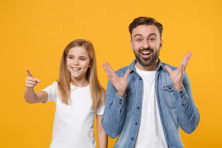 Bearded man in casual clothes with child baby girl. Father little kid daughter isolated on yellow background. Love family day parenthood childhood concept. Pointing index finger aside spreading hands.の写真素材