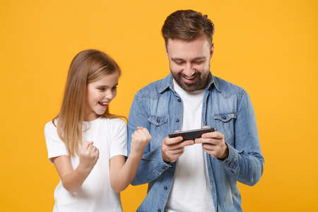 Funny bearded man with cute child baby girl. Father little kid daughter isolated on yellow background. Love family day parenthood childhood concept. Play game with mobile phone, doing winner gesture.の写真素材