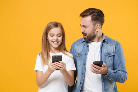Perplexed bearded man in casual clothes with child baby girl. Father little kid daughter isolated on yellow background. Love family day parenthood childhood concept. Use mobile phone type sms message.の写真素材