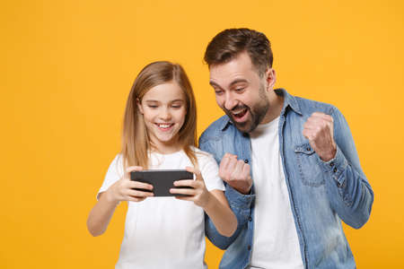 Funny bearded man with cute child baby girl. Father little kid daughter isolated on yellow background. Love family day parenthood childhood concept. Play game with mobile phone, doing winner gesture.の写真素材