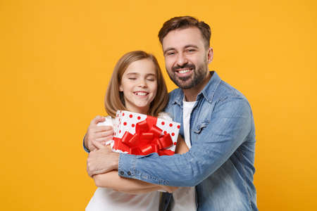 Smiling bearded man with cute child baby girl. Father little kid daughter isolated on yellow background. Love family day parenthood childhood concept. Hold present box with gift ribbon bow, hugging.の写真素材