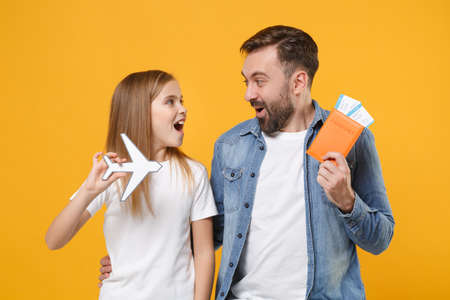 Excited bearded man in casual clothes with child baby girl. Father little kid daughter isolated on yellow background. Love family day parenthood childhood concept. Hold passport tickets air plane.の写真素材