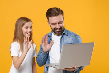 Funny bearded man with child baby girl. Father little kid daughter isolated on yellow background. Love family day parenthood childhood. Hold laptop pc computer, making video call, greeting with hand.の写真素材