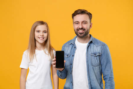 Smiling bearded man have fun with child baby girl. Father little kid daughter isolated on yellow background. Love family day parenthood childhood concept. Hold mobile phone with blank empty screen.の写真素材