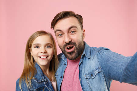 Close up of excited bearded man with cute child baby girl. Father little kid daughter isolated on pastel pink background. Love family parenthood childhood concept. Doing selfie shot on mobile phone.の写真素材