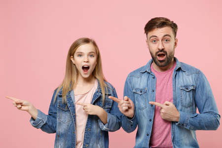 Shocked bearded man in casual clothes with cute child baby girl. Father little kid daughter isolated on pastel pink background. Love family parenthood childhood concept. Pointing index fingers aside.の写真素材
