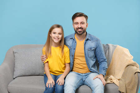 Smiling bearded man in casual clothes have fun with child baby girl. Father little kid daughter isolated on pastel blue background. Love family parenthood childhood concept. Sitting on couch, hugging.の写真素材
