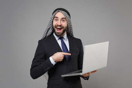 Excited bearded arabian muslim businessman in keffiyeh kafiya ring igal agal suit isolated on gray...