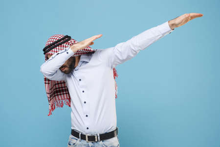 Young bearded arabian muslim man in keffiyeh kafiya ring igal agal casual clothes isolated on pastel blue background. People religious lifestyle concept. Mock up copy space. Showing DAB dance gesture.の写真素材