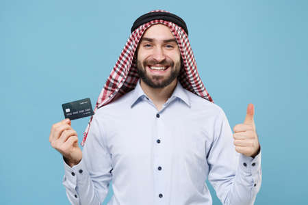 Smiling young bearded arabian muslim man in keffiyeh kafiya ring igal agal casual clothes isolated on pastel blue background.の写真素材