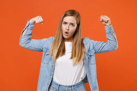 Strong young woman girl in casual denim clothes posing isolated on bright orange wall background studio portrait.の写真素材