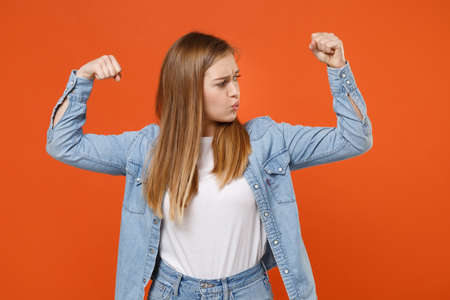 Strong young woman girl in casual denim clothes posing isolated on bright orange wall background studio portrait.の写真素材