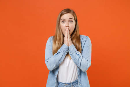 Shocked young woman girl in casual denim clothes posing isolated on orange wall background studio portrait.の写真素材