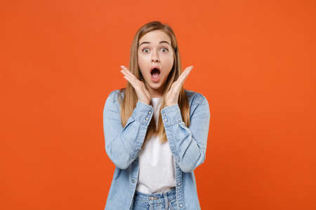 Shocked young woman girl in casual denim clothes posing isolated on orange wall background studio portrait.の写真素材