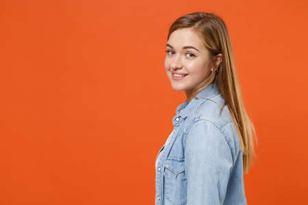 Side view of pretty young woman girl in casual denim clothes posing isolated on orange wall background studio portrait.の写真素材