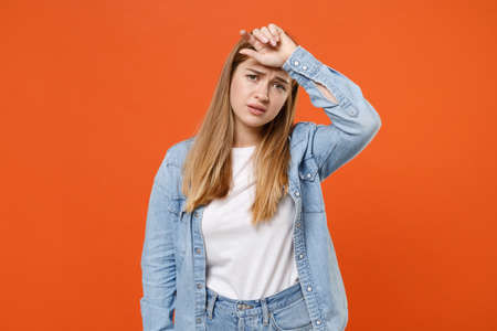 Tired exhausted young woman girl in casual denim clothes posing isolated on orange wall background studio portrait.の写真素材