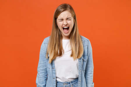 Frustrated young woman girl in casual denim clothes posing isolated on orange background studio portrait.の写真素材