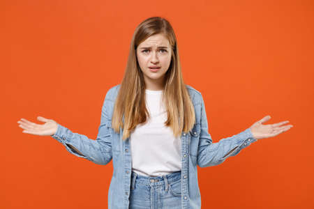 Perplexed puzzled young woman girl in casual denim clothes posing isolated on orange wall background studio portrait.の写真素材