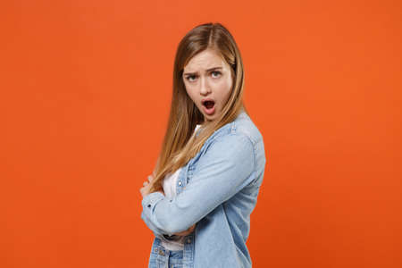 Side view of shocked perplexed young woman girl in casual denim clothes posing isolated on orange wall background.の写真素材