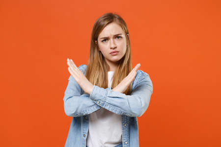 Dissatisfied young woman girl in casual denim clothes posing isolated on orange wall background studio portrait.の写真素材