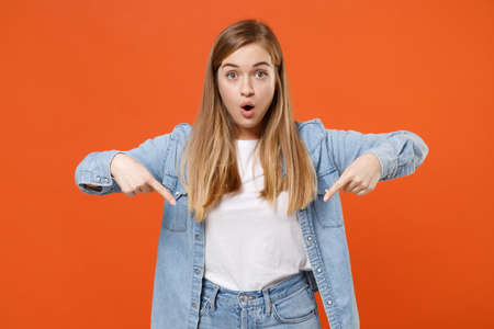 Shocked young woman girl in casual denim clothes posing isolated on orange wall background studio portraitの写真素材