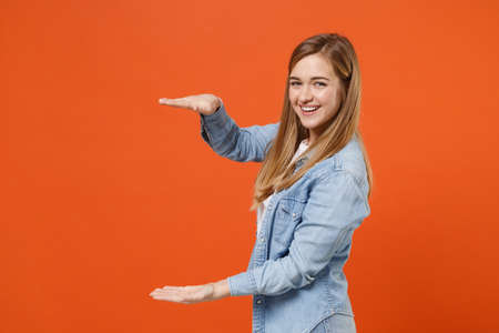 Smiling young woman girl in casual denim clothes posing isolated on orange background in studio.の写真素材
