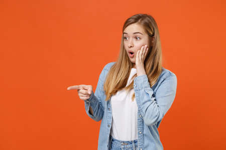 Shocked young woman girl in casual denim clothes posing isolated on orange wall background studio portrait.の写真素材