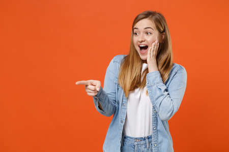 Excited young woman girl in casual denim clothes posing isolated on orange wall background studio portrait.の写真素材