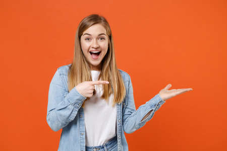 Surprised young woman girl in casual denim clothes posing isolated on orange background studio portrait.の写真素材