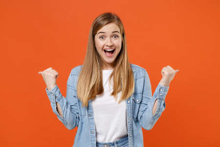 Excited surprised young woman girl in casual denim clothes posing isolated on orange background studio portrait.の写真素材