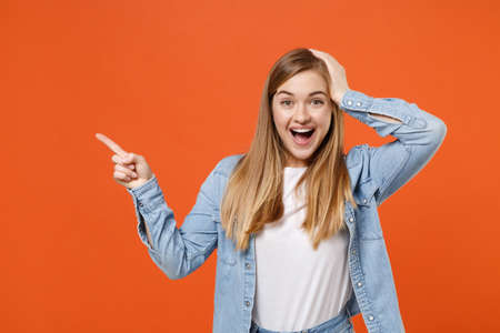 Excited young woman girl in casual denim clothes posing isolated on orange wall background studio portrait.の写真素材