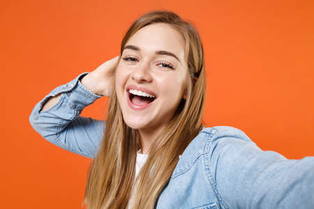 Close up of cheerful young woman girl in casual denim clothes posing isolated on orange background.の写真素材