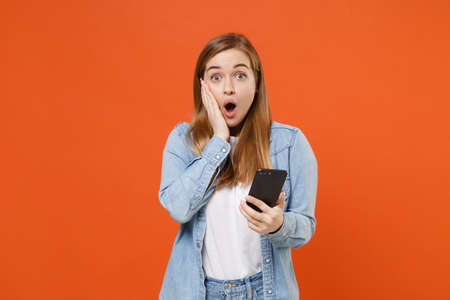 Shocked young woman girl in casual denim clothes posing isolated on bright orange wall background...